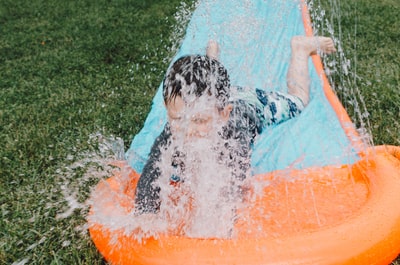白天，儿童在蓝色和橙色滑垫上滑倒，溅起水花
